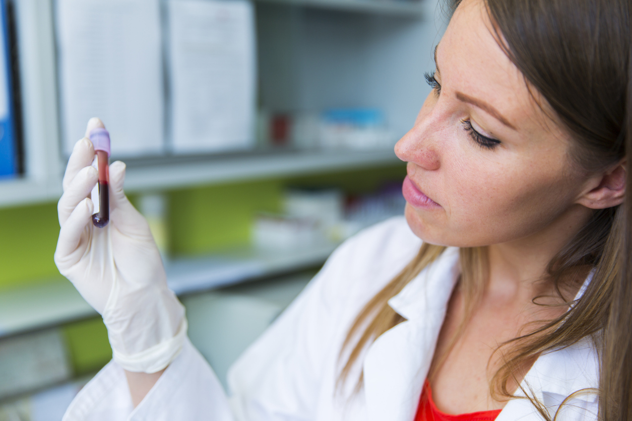 A doctor examines a vial of a blood sample in her hand.