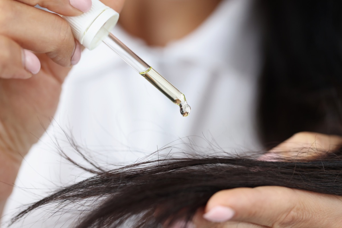 Close-up of girl hold dropper with castor extract oil near hair and apply one drop. Long hair care routine, oil for head. Wellness, beauty ritual concept