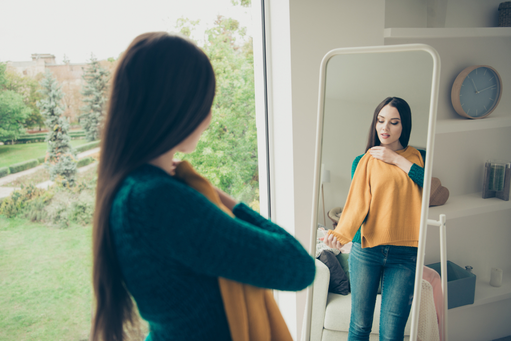 Young woman trying on yellow sweater in mirror