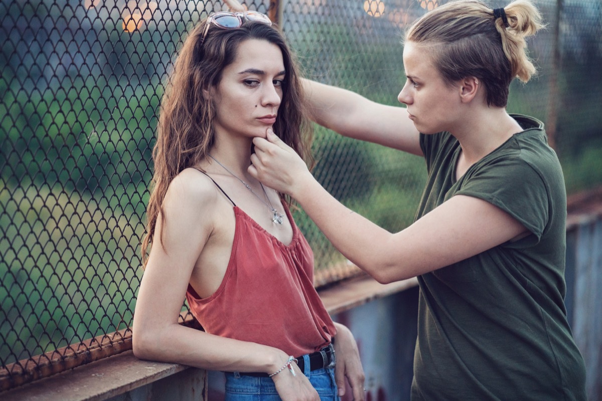 Woman consoling and holding the chin of her girlfriend or wife as they stand on pedestrian bridge during an argument