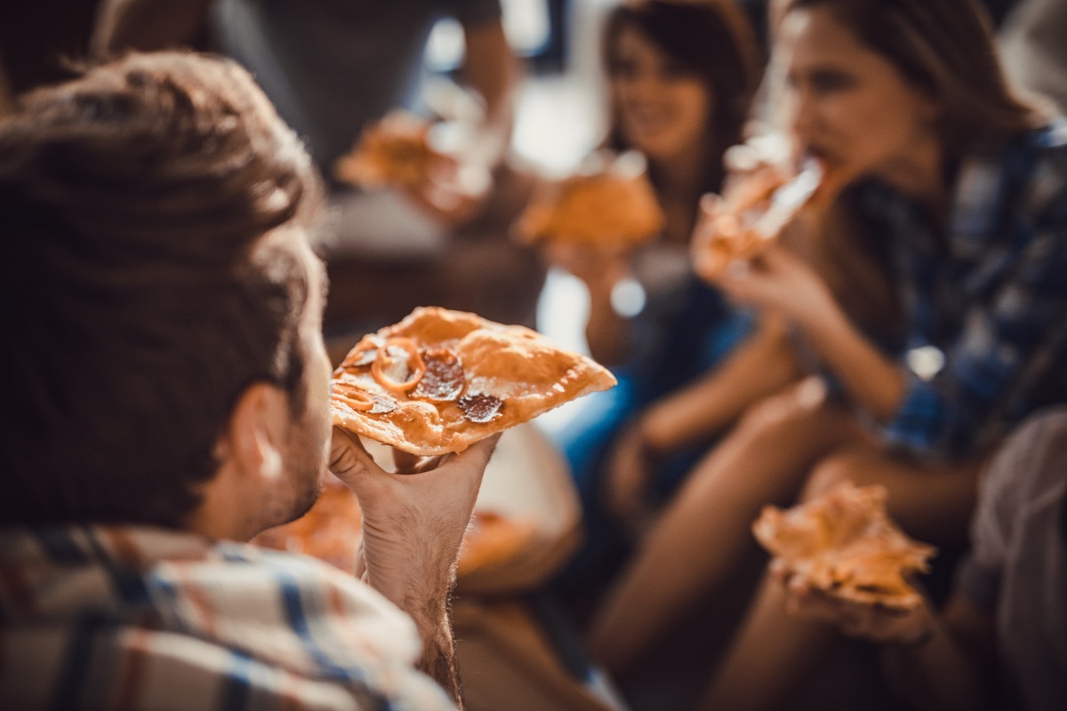 Man eating pizza for lunch with his friends. Focus is on human hand and pizza slice.