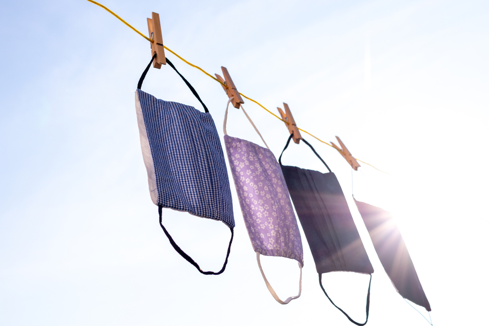 Four cloth face masks hanging in bright sunlight on a clothesline