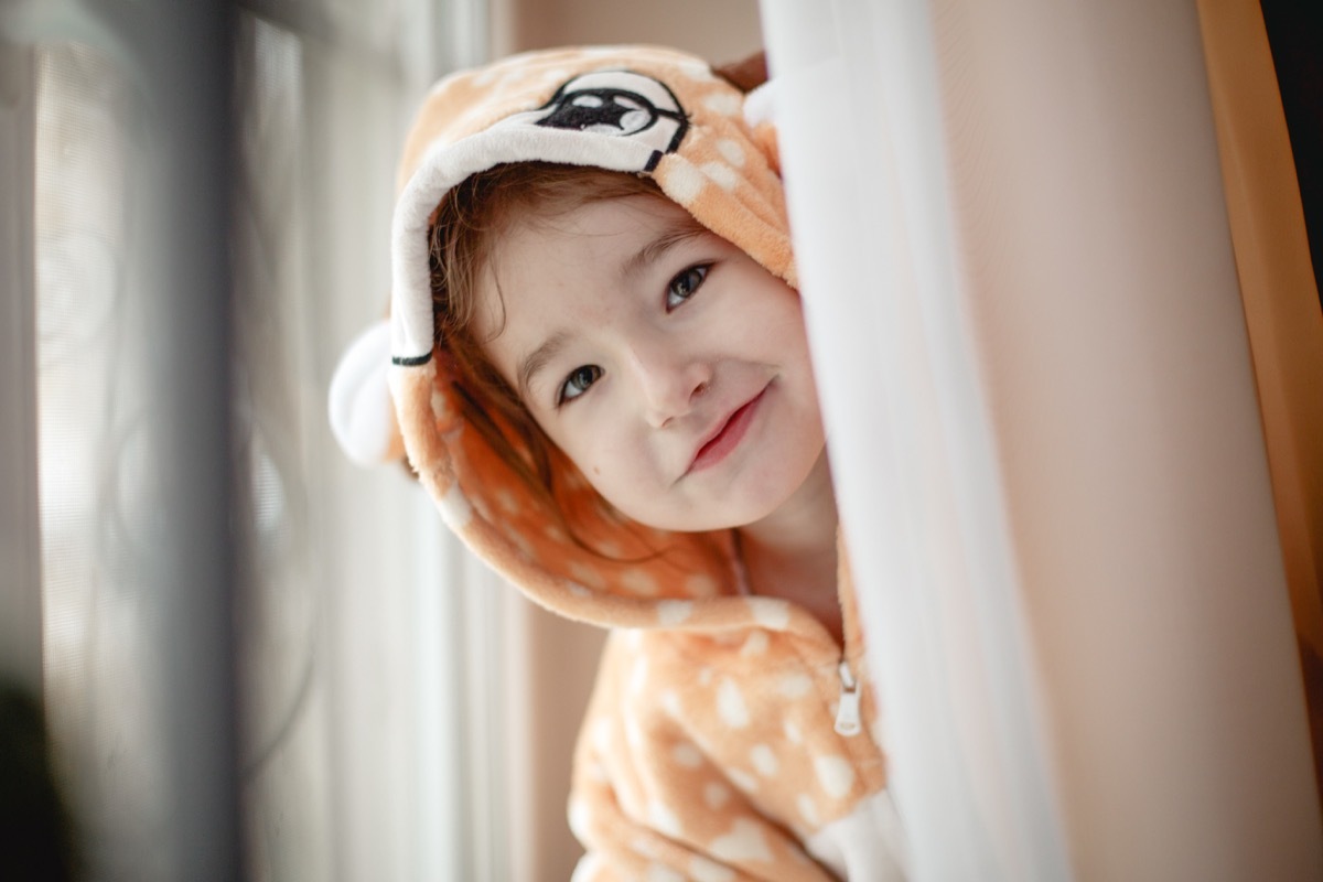 little girl in bathrobe peeking from behind curtain