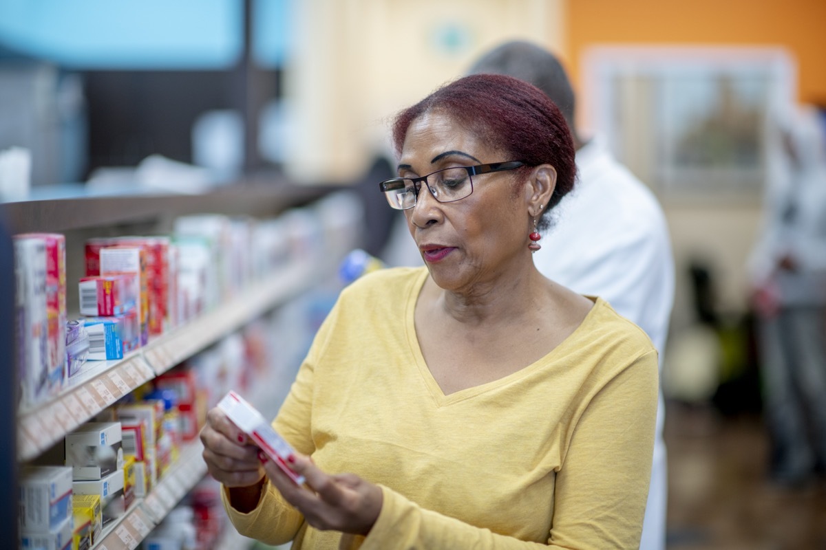 A woman peruses the shelf at a pharmacy, reading the label.