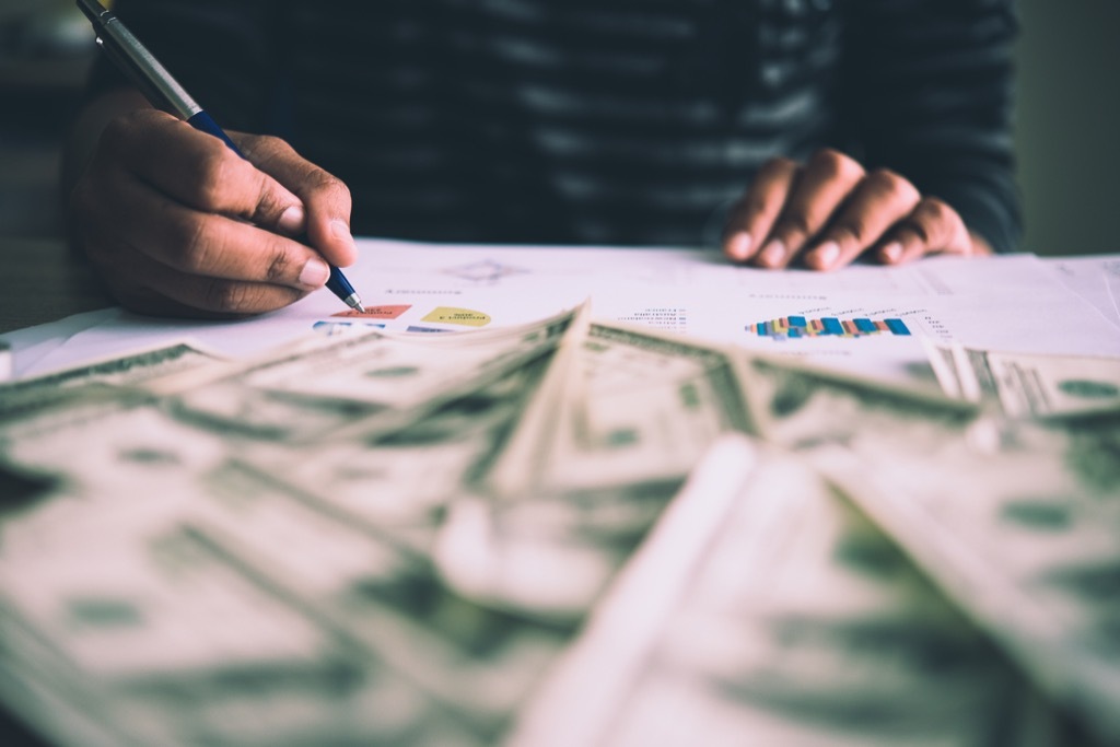 black man's hands filling out financial paperwork with a stack of money in front of him