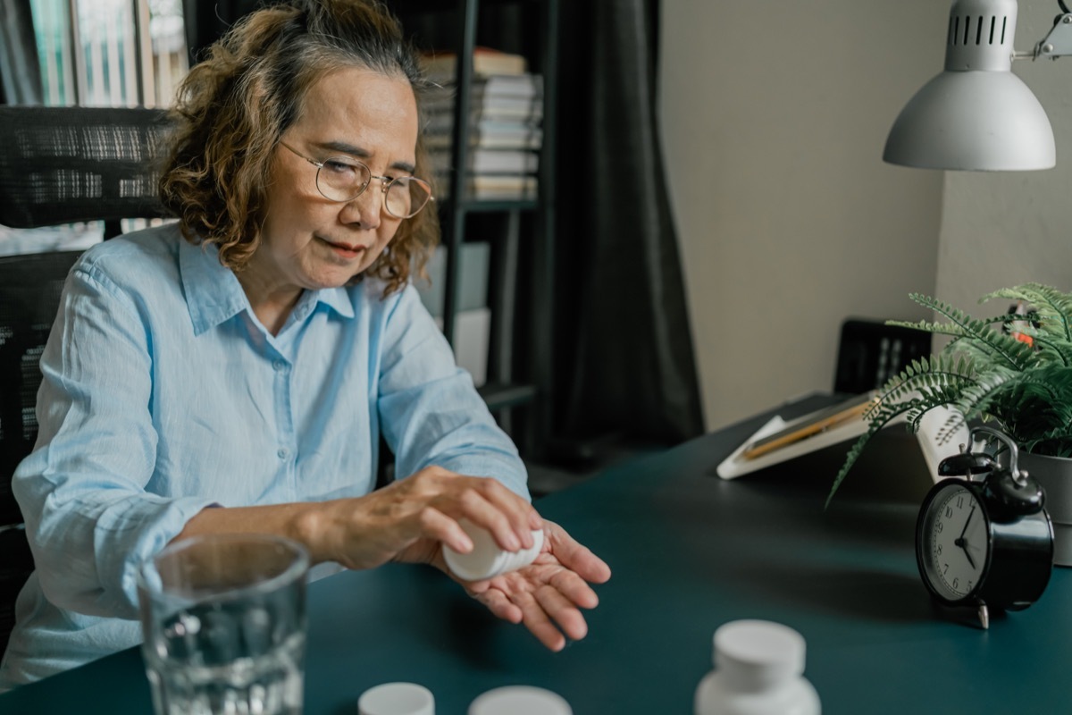 Senior woman taking pill and Video call consulting with doctor asking for medicine description on laptop computer while sitting on kitchen table at home. Video Conference