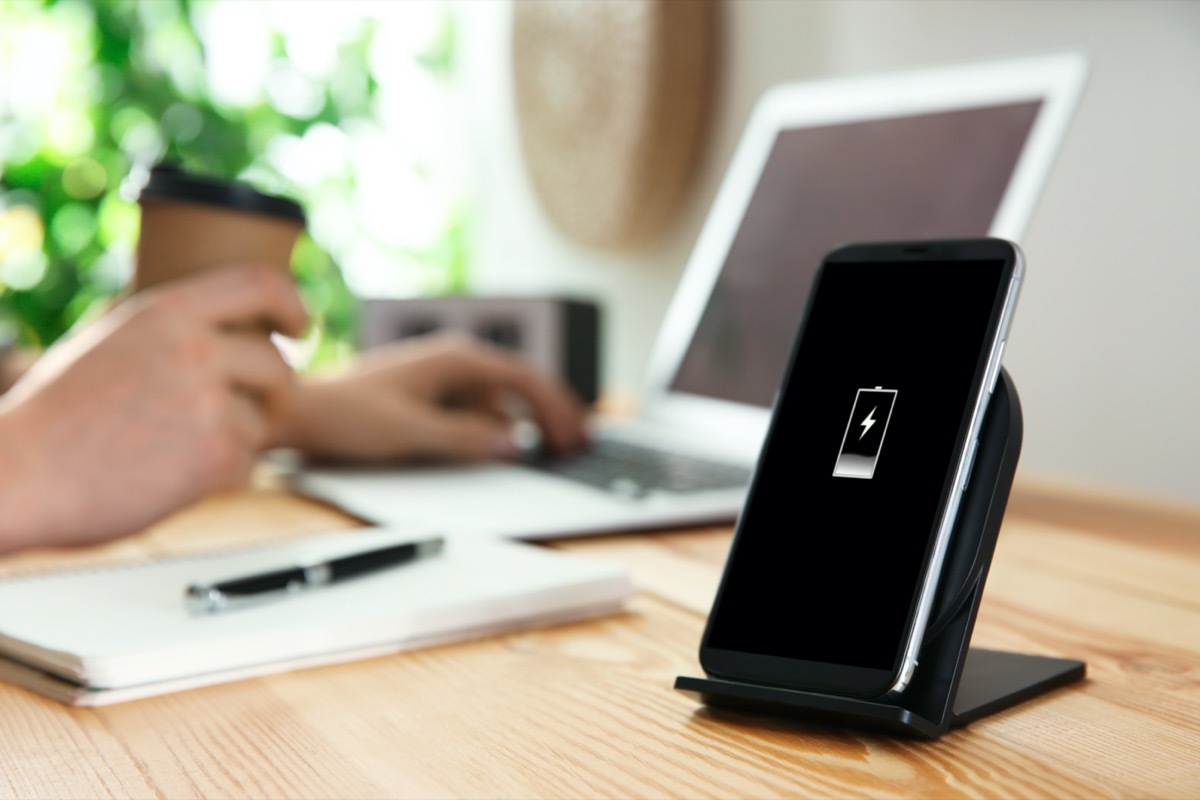 black contact phone charger on wooden desk next to person working on laptop