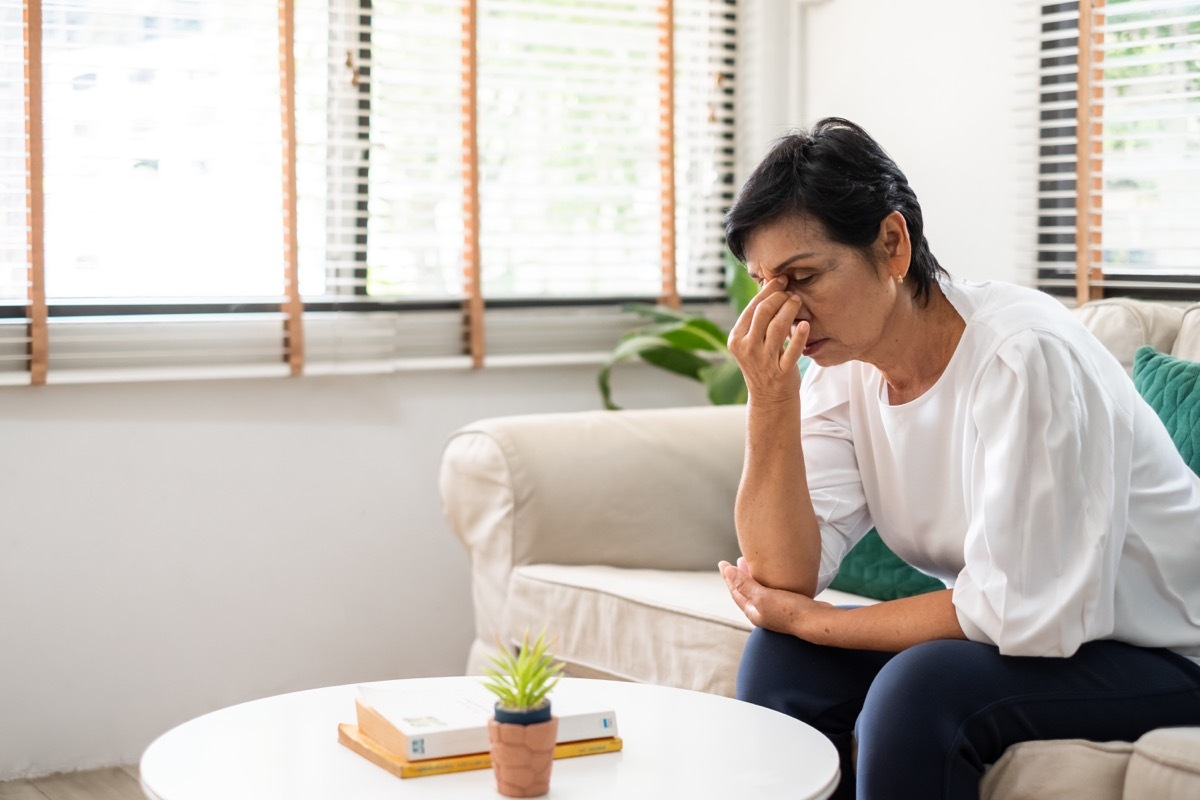 woman feel stressed, headache sitting alone on sofa at home