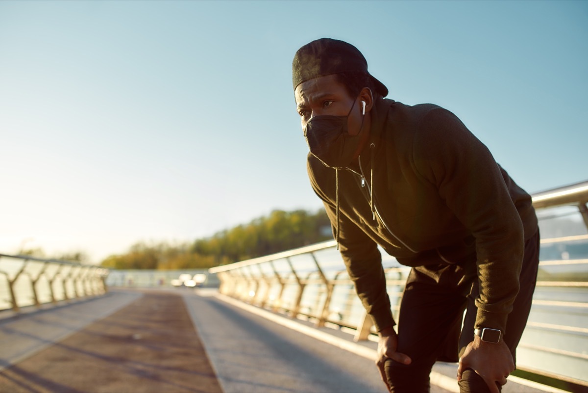 tired jogger in protective mask resting after running while standing on the bridge in the morning. Running at sunrise. Sport during quarantine. Covid-19. Protection. Staying active