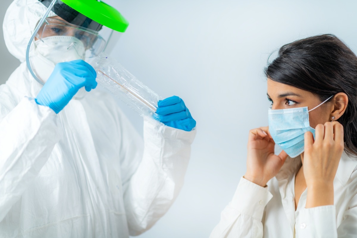 Medical worker in protective suite taking a swab for corona virus test, potentially infected young woman