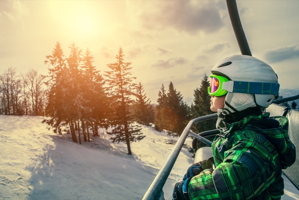 young boy in helmet, goggles, and skit coat sits in a chairlift with a snow-covered mountain behind him, state fact about idaho