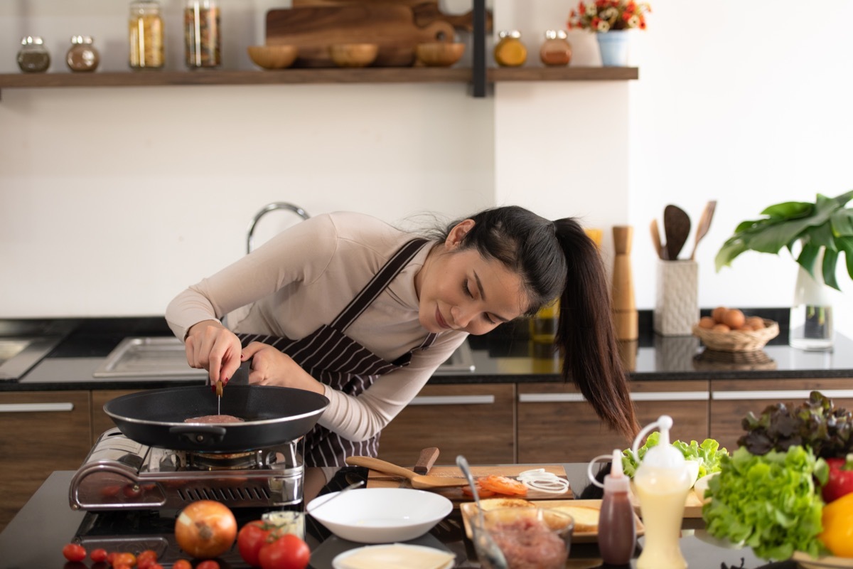 young woman cooking meat in a pan in modern kitchen