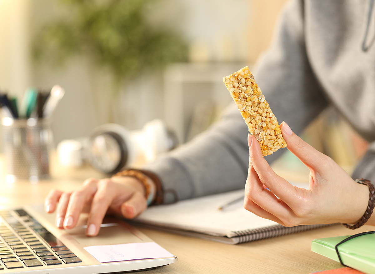 eating a protein bar at a desk with a laptop