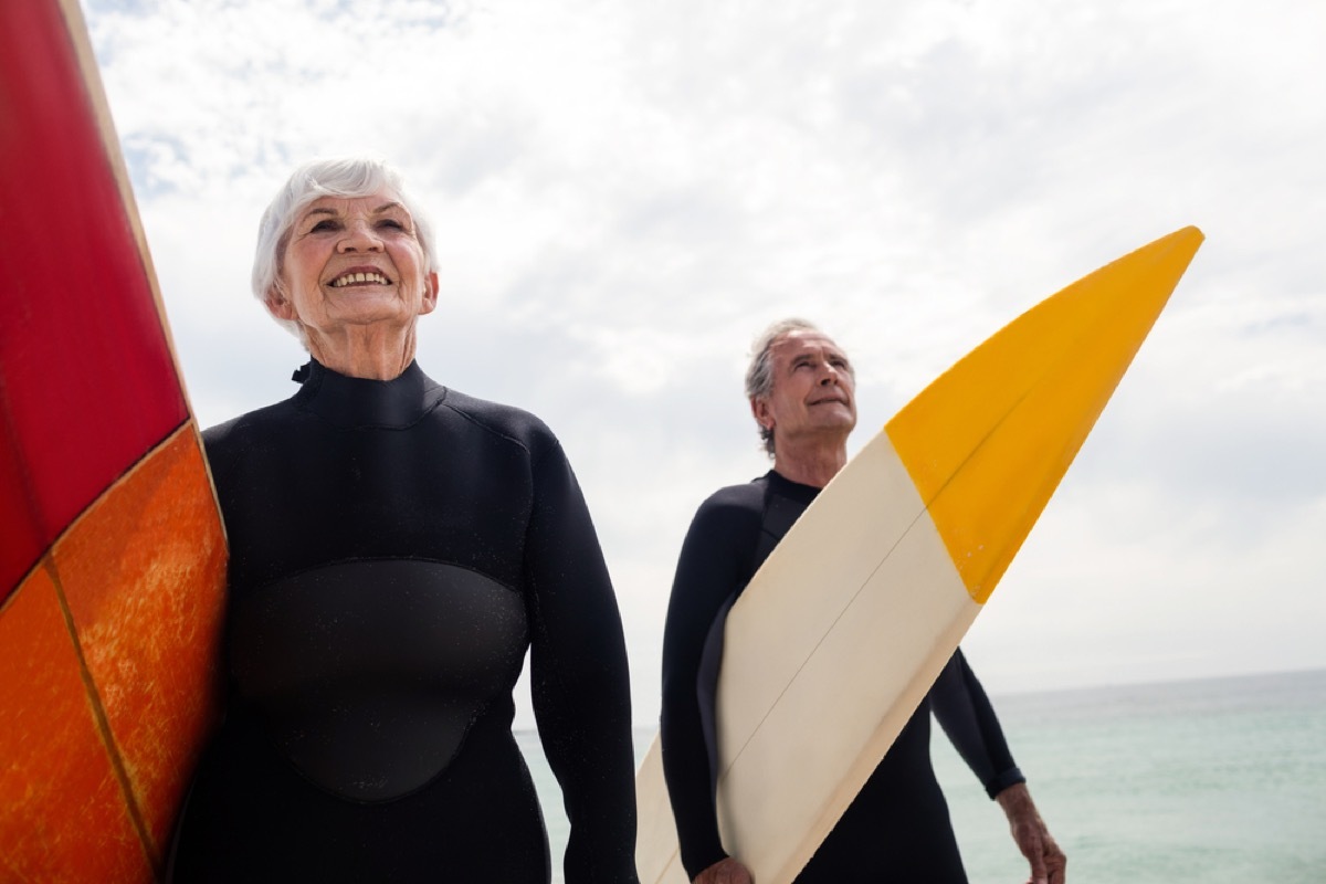 older couple on the beach in wetsuits with surfboards, better wife after 40