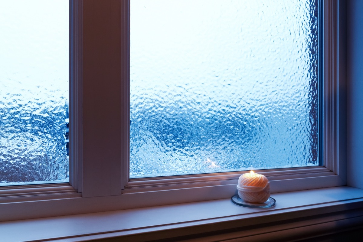 Cozy candle burning near a frosted window. Winter evening.