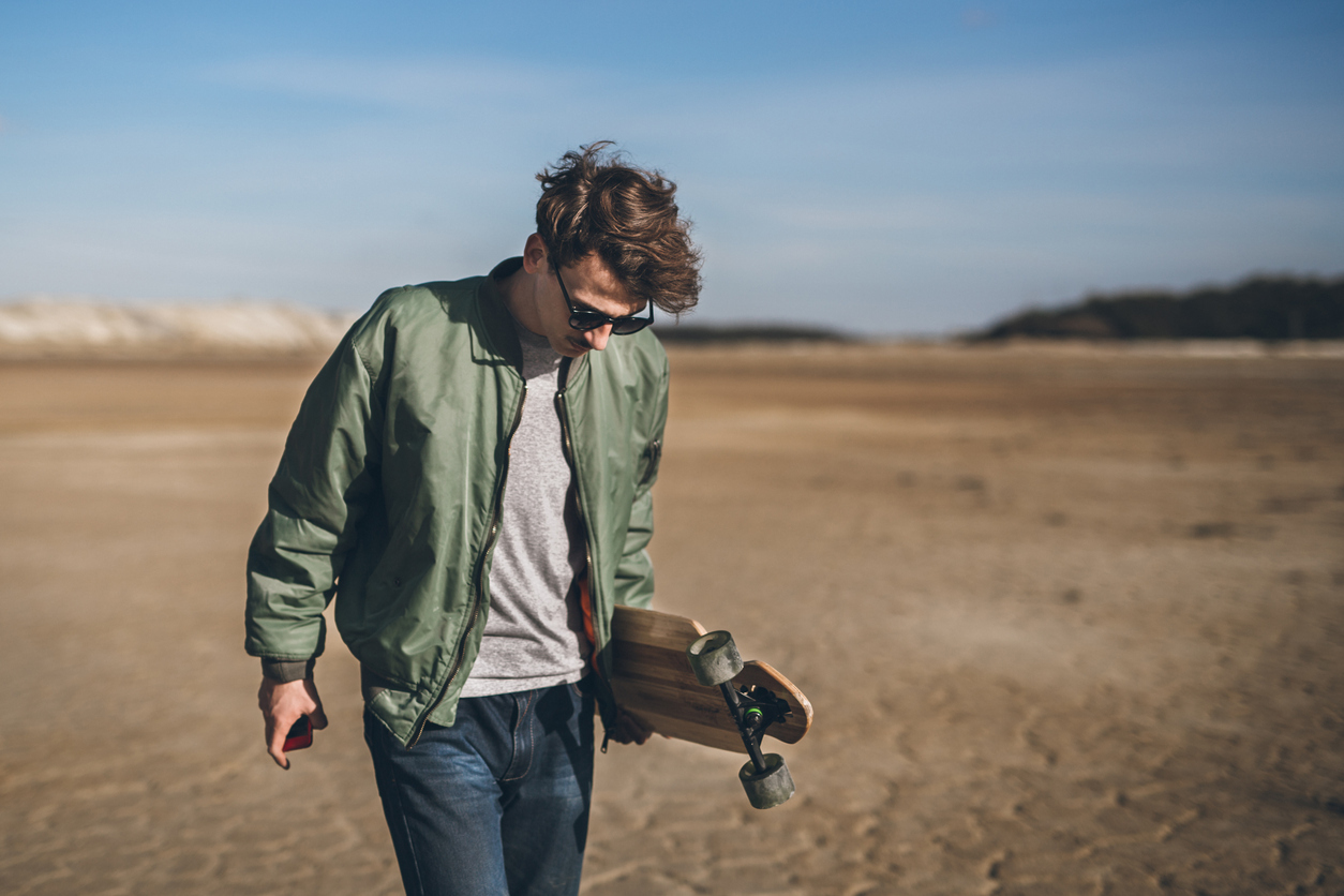 Young rebelious skater with his board, walking alone in a bomber jacket