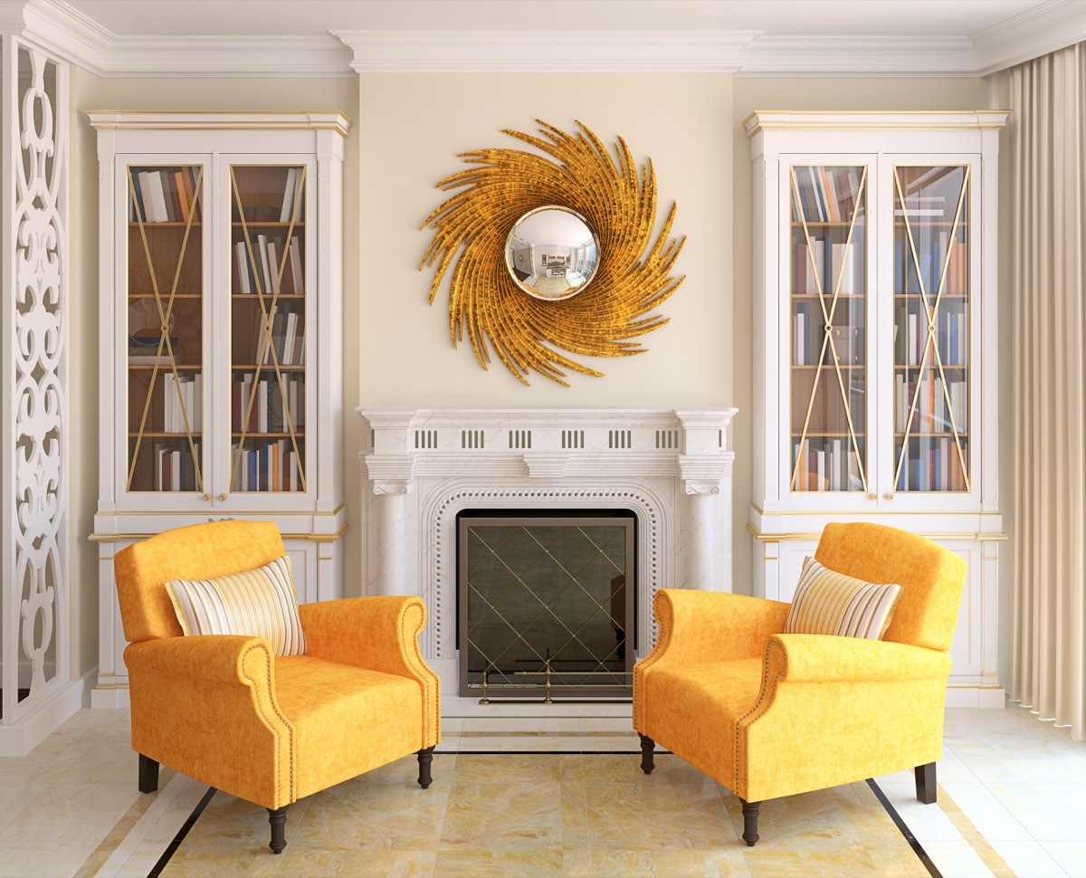 Yellow chairs and a sunburst mirror in a living room with a fireplace