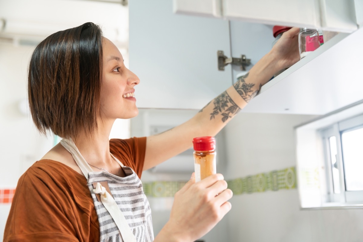 woman cooking at home and looking for some spices in the kitchen cabinet