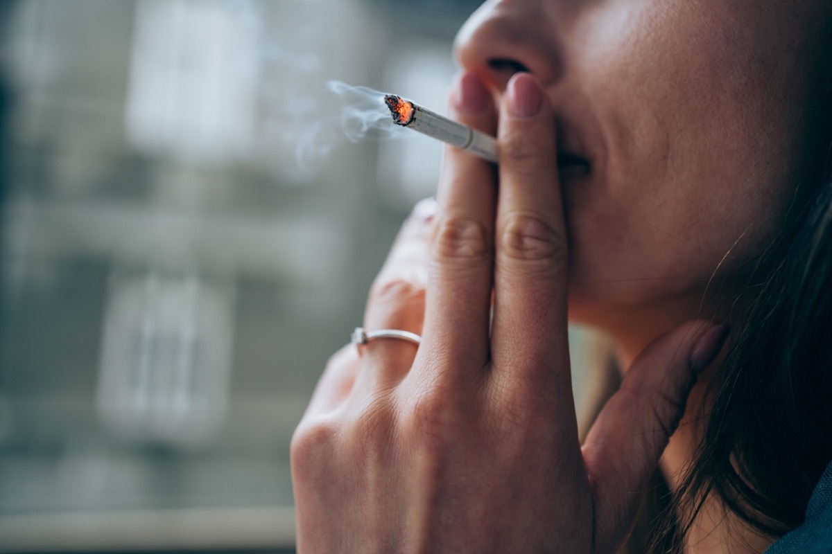 Unrecognizable young woman enjoying a cigarette outdoors. Focus is on the cigarette.