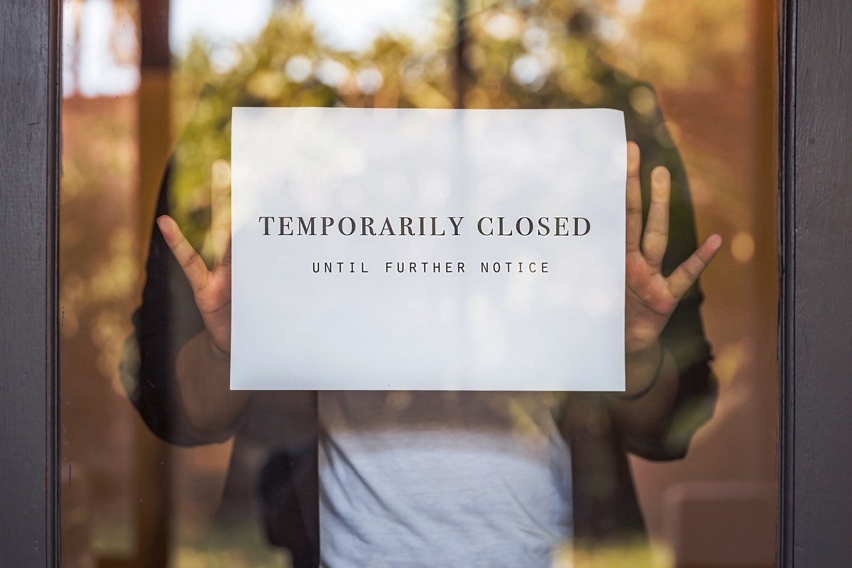 Portrait shot of retail store manager putting a temporarily closed sign, in front of her store window during Covid 19 pandemic