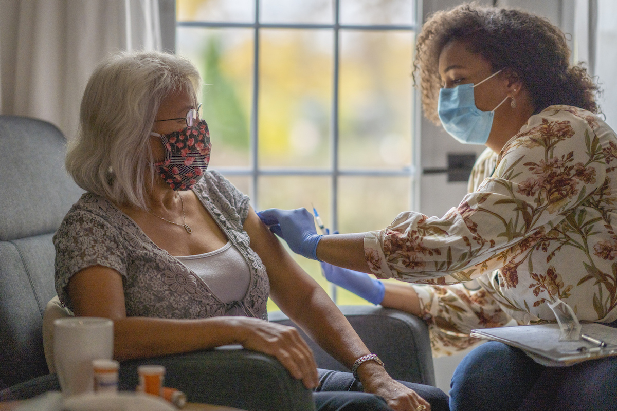 Senior woman getting a vaccine from her doctor in her home during a house visit during the COVID-19 pandemic.