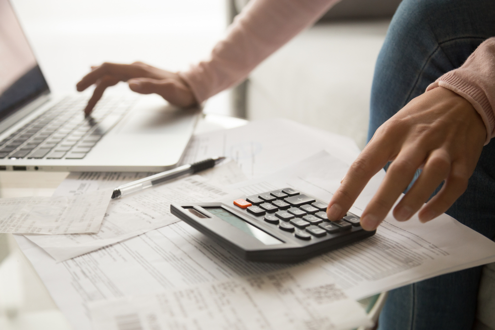 A closeup of someone using a calculator while inputing information onto a laptop