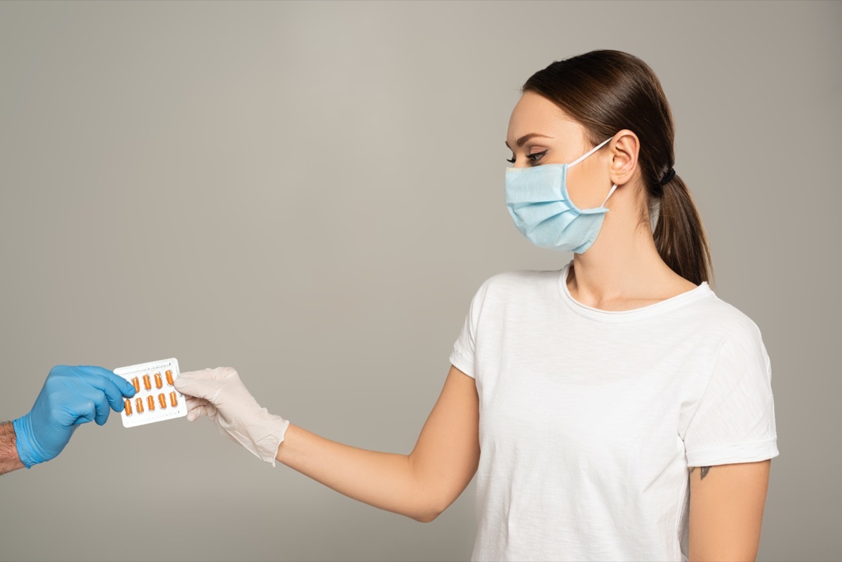 Woman in medical mask holding blister with pills near man in latex glove