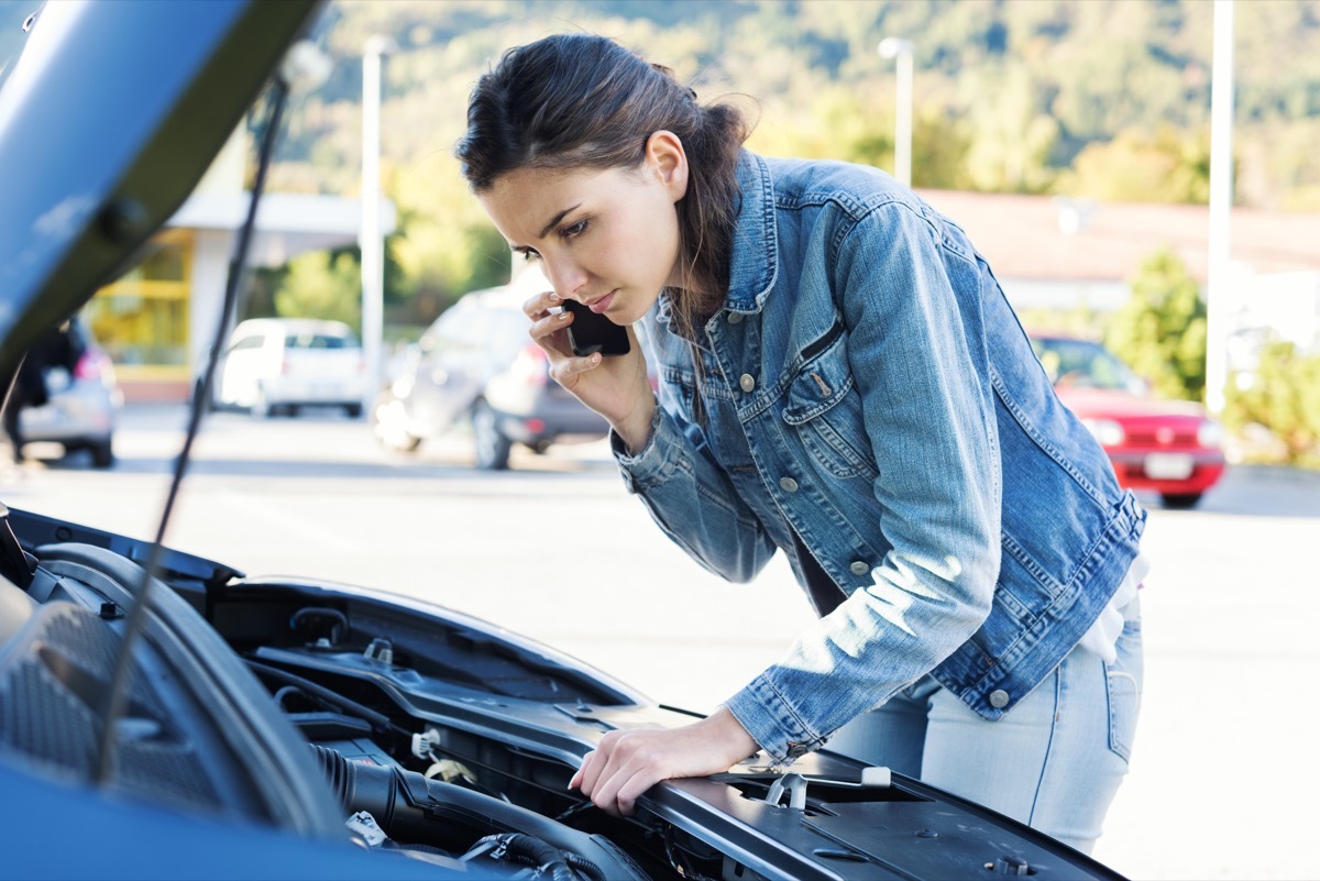 Young woman calling a car assistance service with her smartphone, her car has broken down