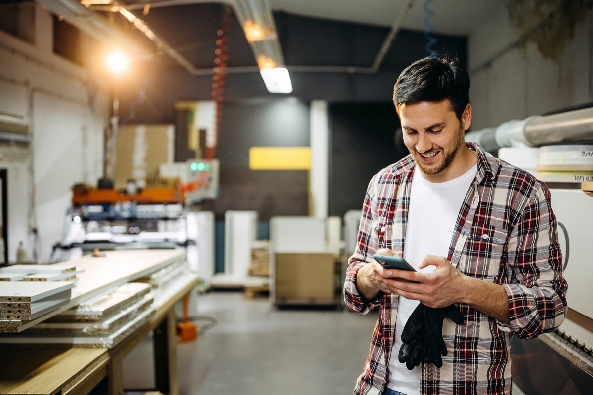 Young smiling casually clothed carpenter using phone