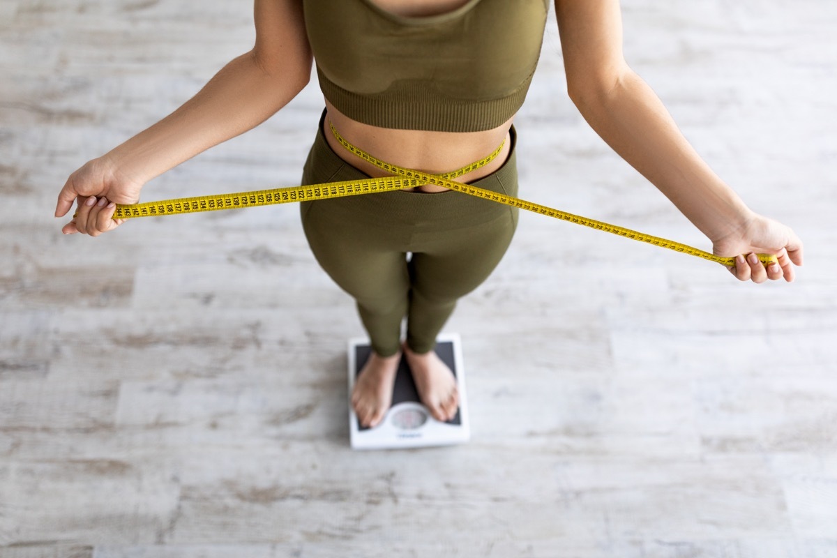 woman measuring waist while standing on scale