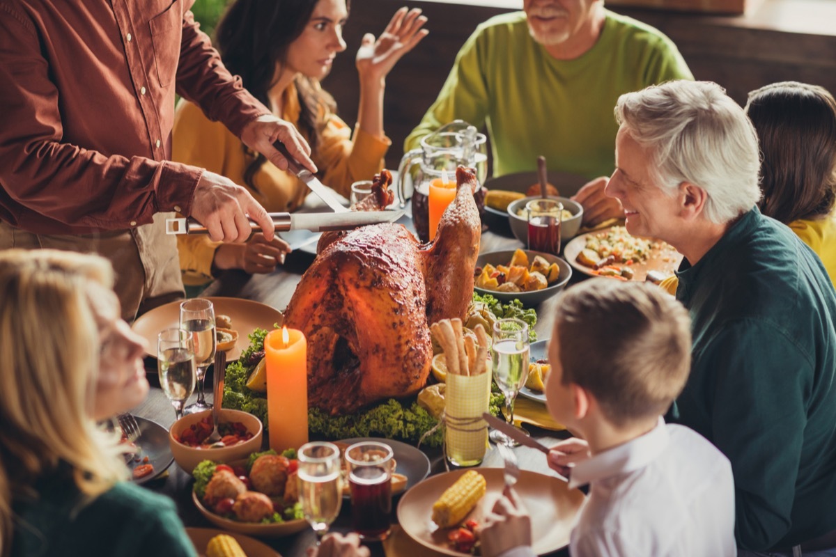 Cropped photo of family meeting, served table thanks giving dinner two knives slicing stuffed turkey meal living room indoors