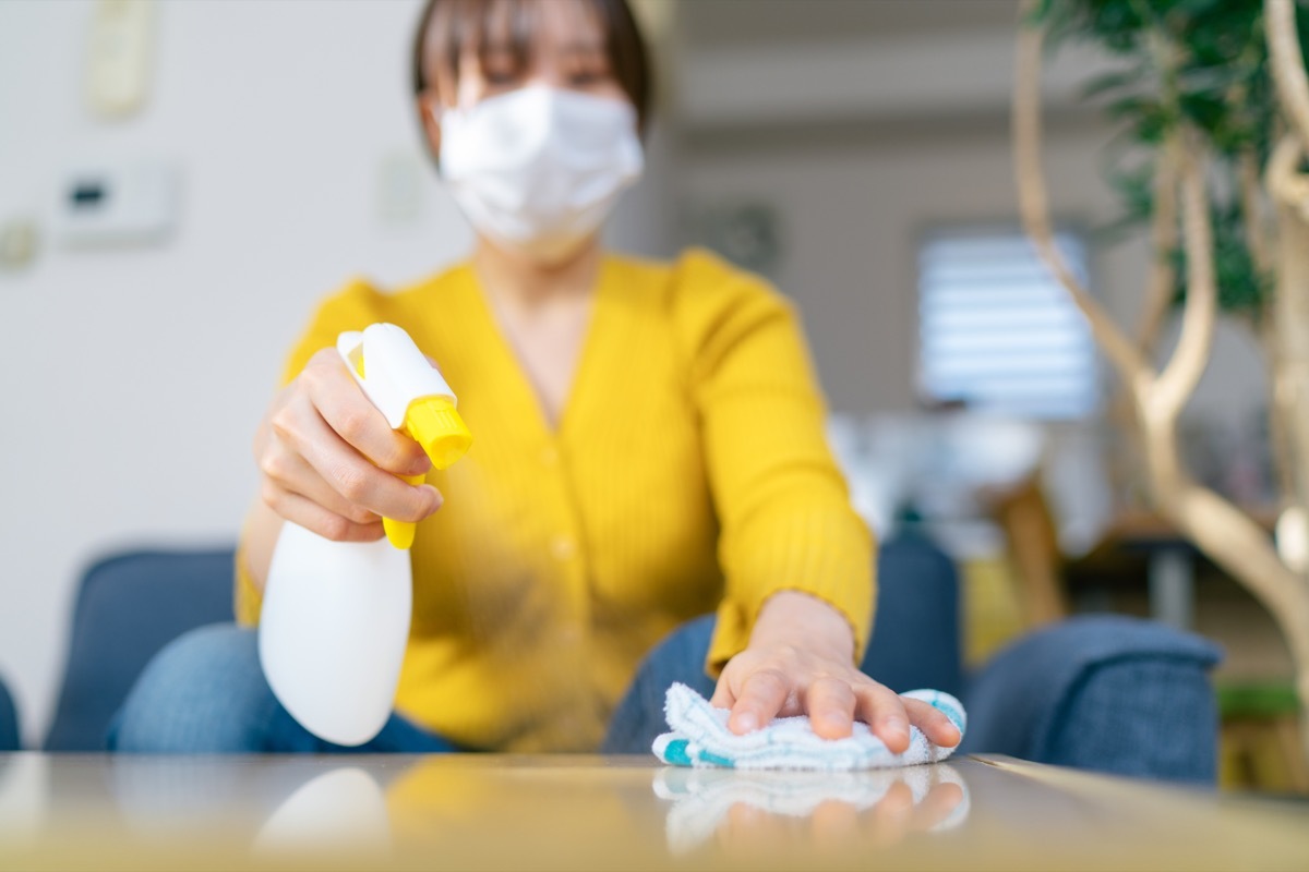 A young woman is wiping a desk surface with alcohol spray.