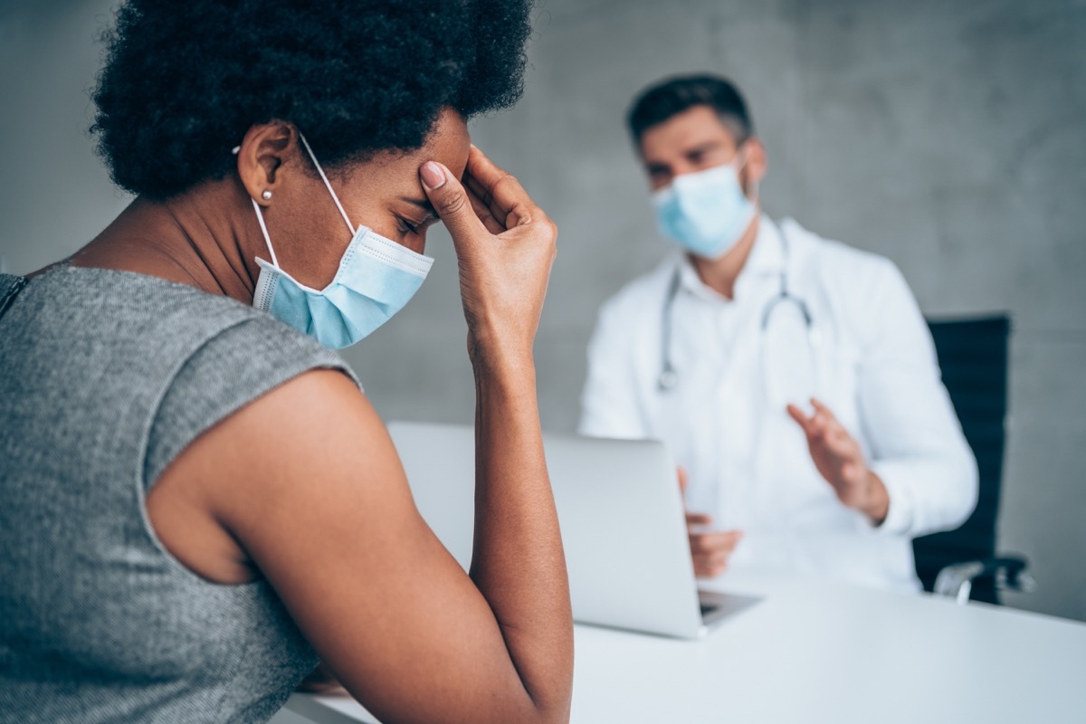 woman sitting opposite the doctor in his office and holding her head with hand.