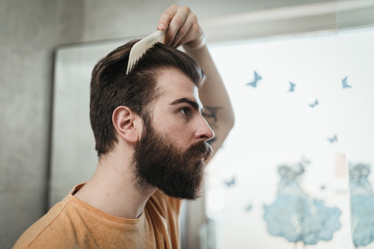 man combing hair while looking in the mirror