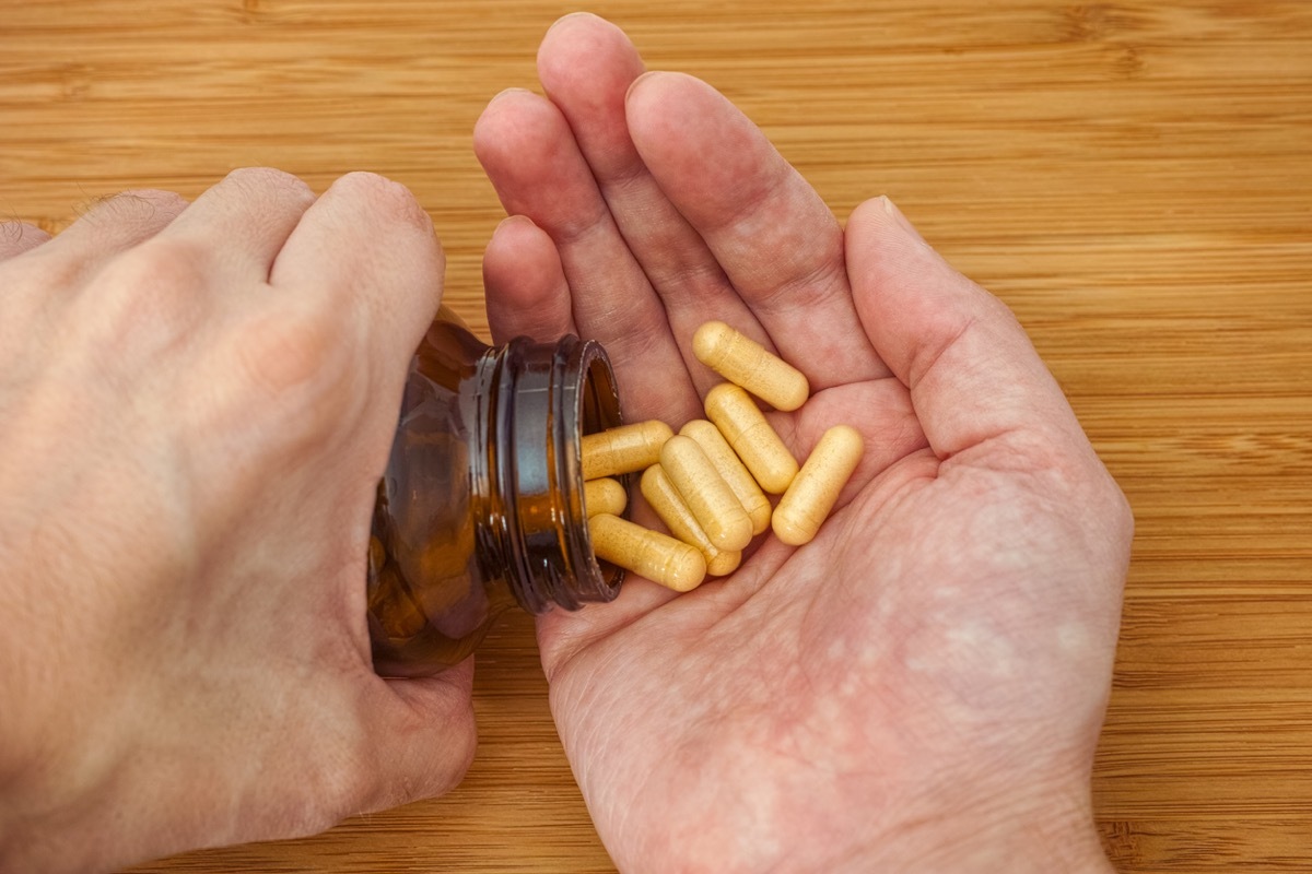 Person taking Vitamin B Complex pills out of a bottle. Close up.