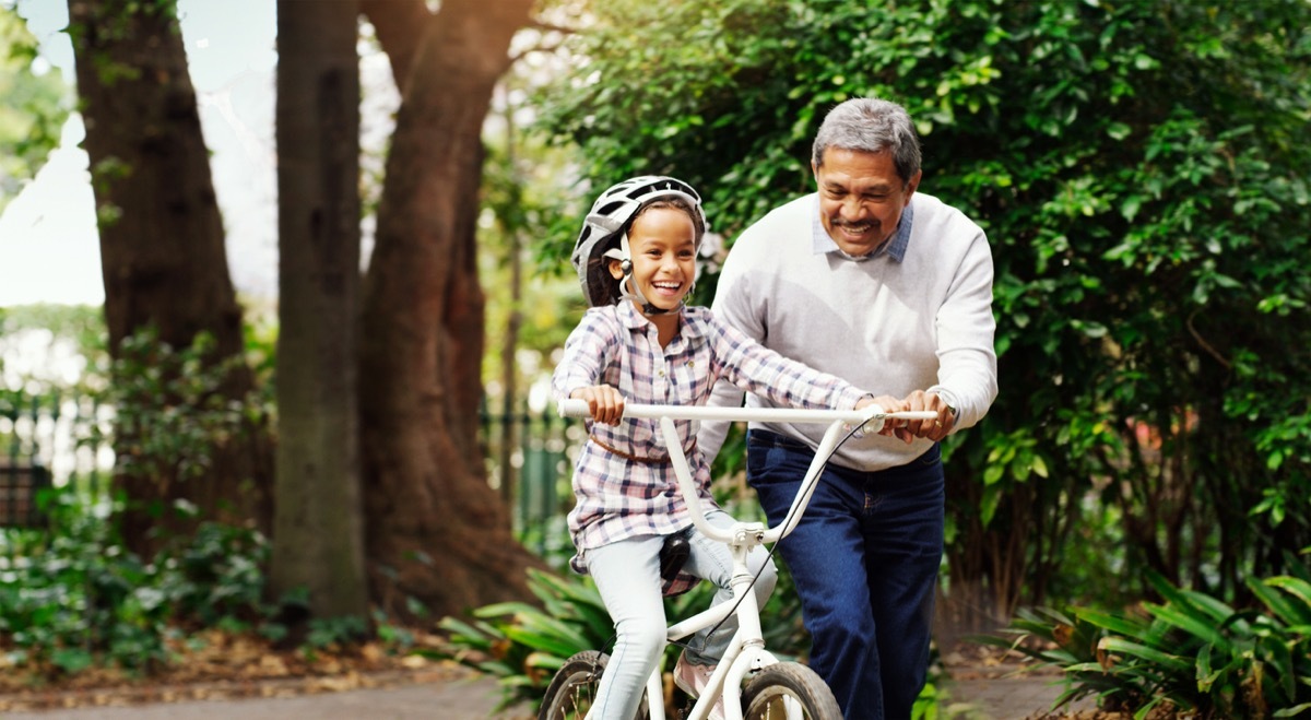 grandparent teaching his granddaughter how to ride a bike outside