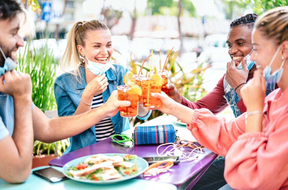 Friends drinking spritz at cocktail bar with face masks