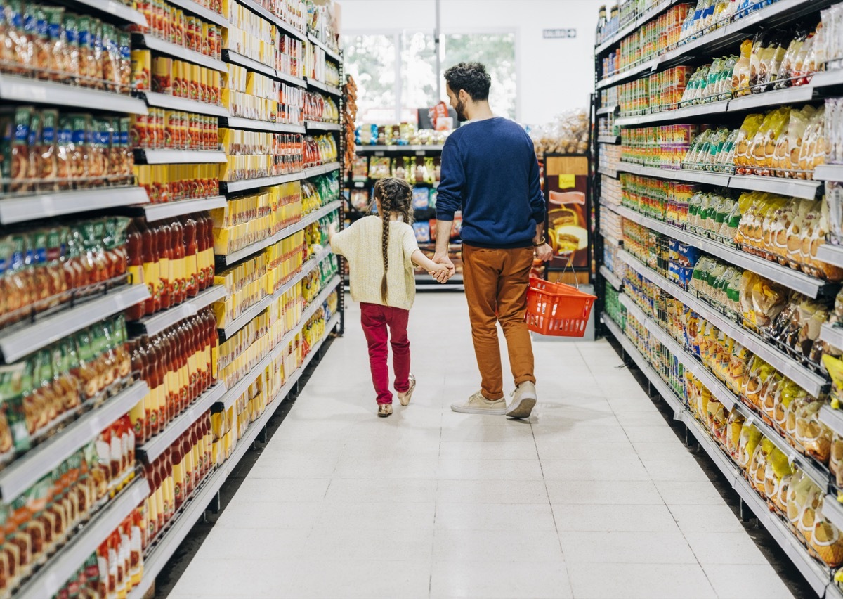 Father and daughter shopping at grocery store. Family is at supermarket. They are holding hands while walking at aisle.