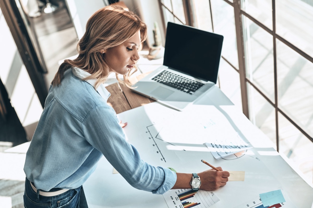 woman writing on a post-it note by a laptop at a drafting table - handwriting analysis