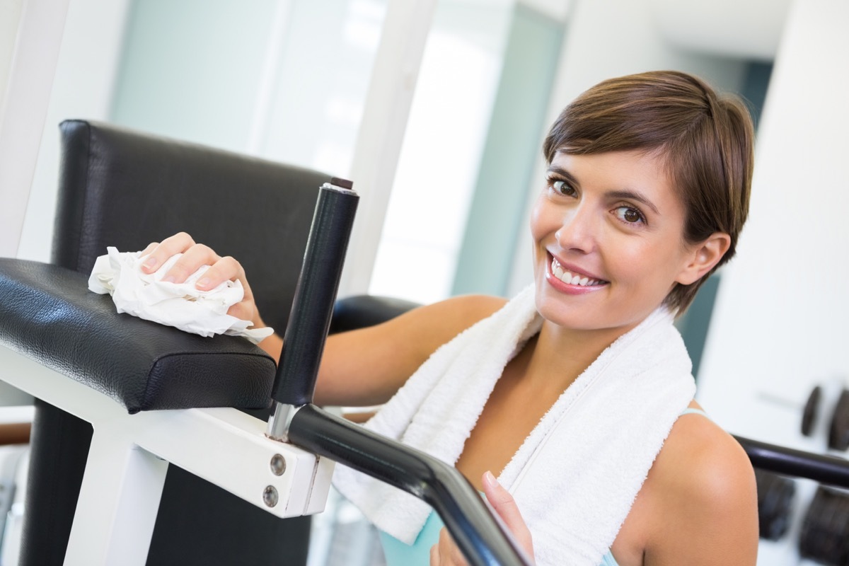 wiping down bench smiling at camera at the gym