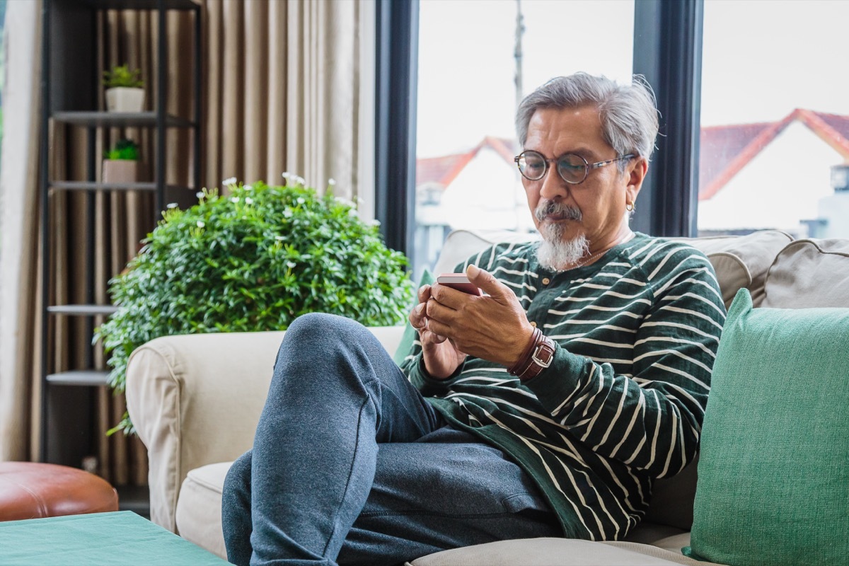 senior man using smart phone while sitting on sofa