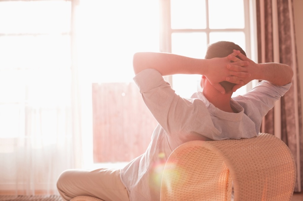 man sits back in chair, photographed from behind, with hands behind his head as he relaxes