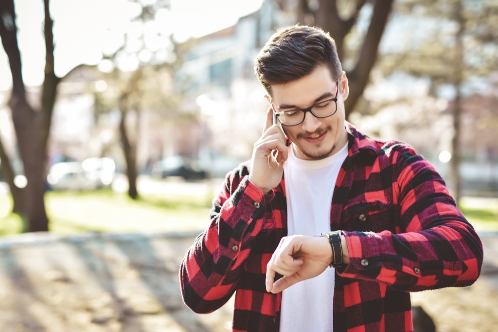 Man wearing a red and black plaid shirt checking his watch while talking on the phone