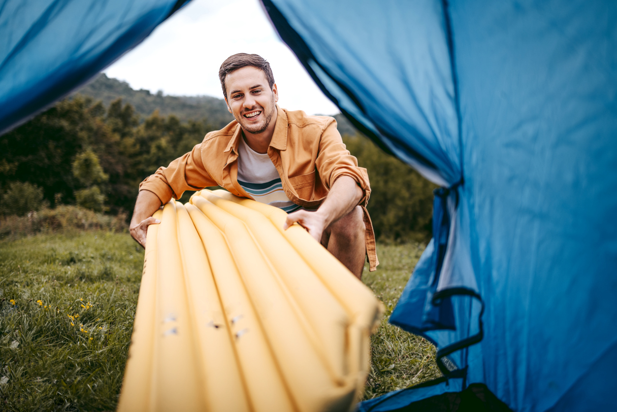 Young handsome camper setting up his air bad for camping