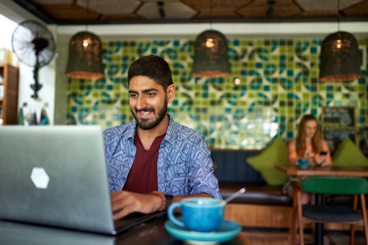 young indian man working on a laptop at a coffee shop