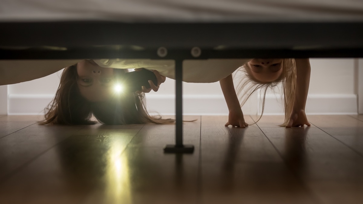 mother and daughter looking under bed with flashlight