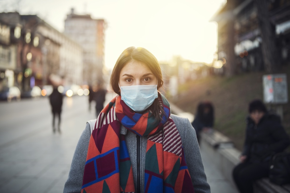 Portrait of young woman with protective face mask on the street, looking at camera