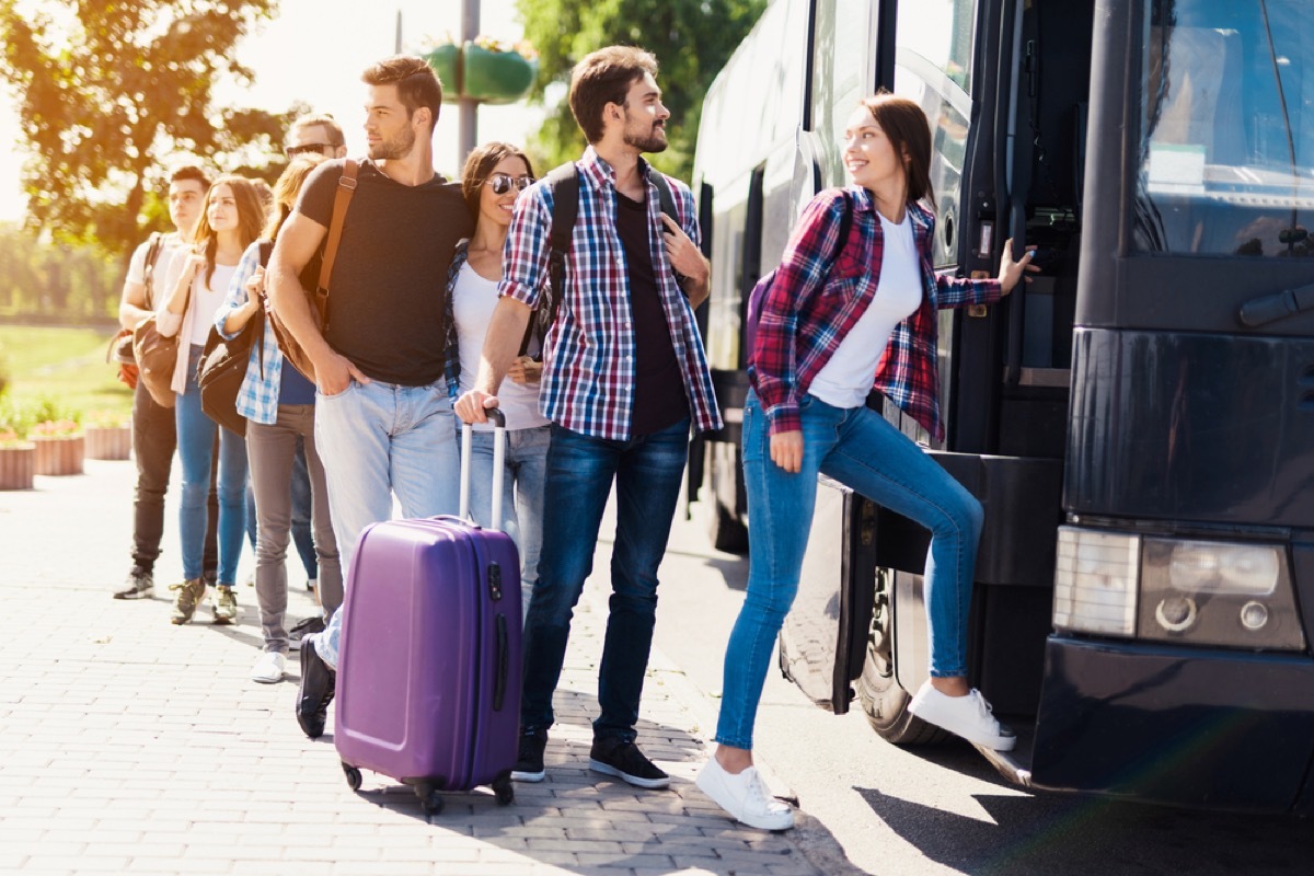 a line of tourists getting on a bus with suitcases