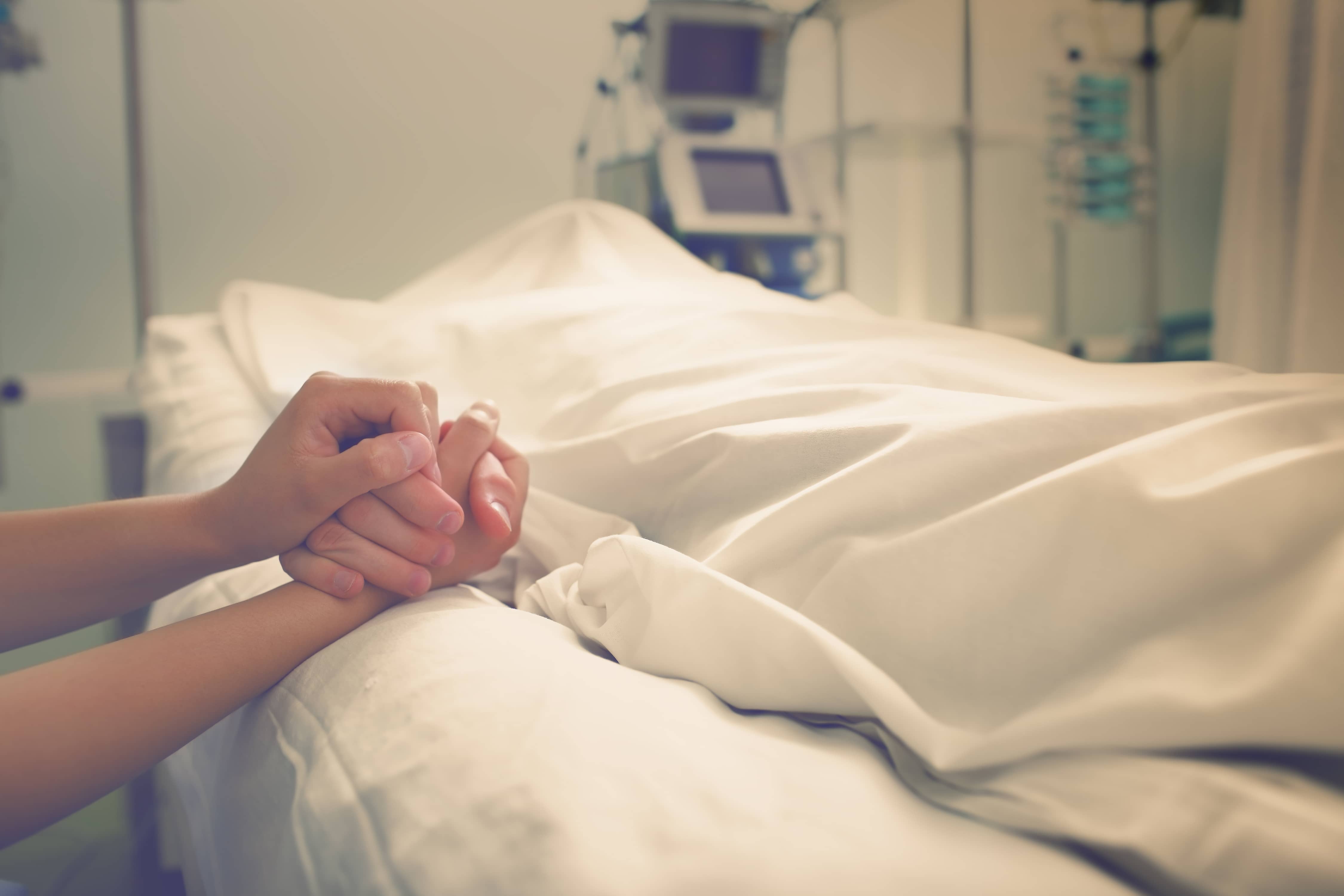 family holding hands over a hospital bed