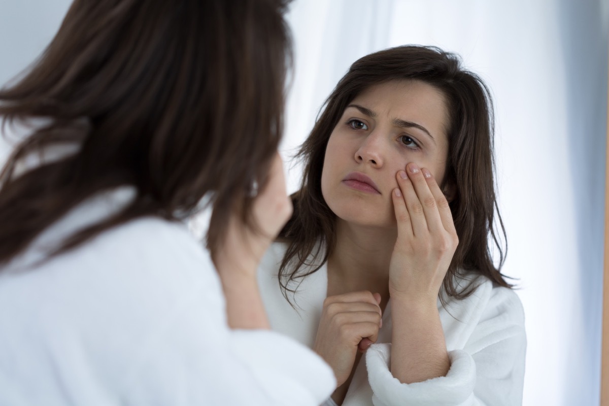 young woman looking concerned with her hand by her eye in mirror